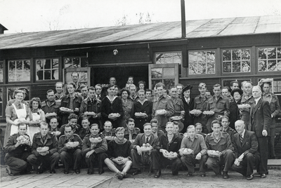 502564 Groepsportret van een onbekend gezelschap (dienstplichtigen?) die een fruitmand aangeboden hebben gekregen.